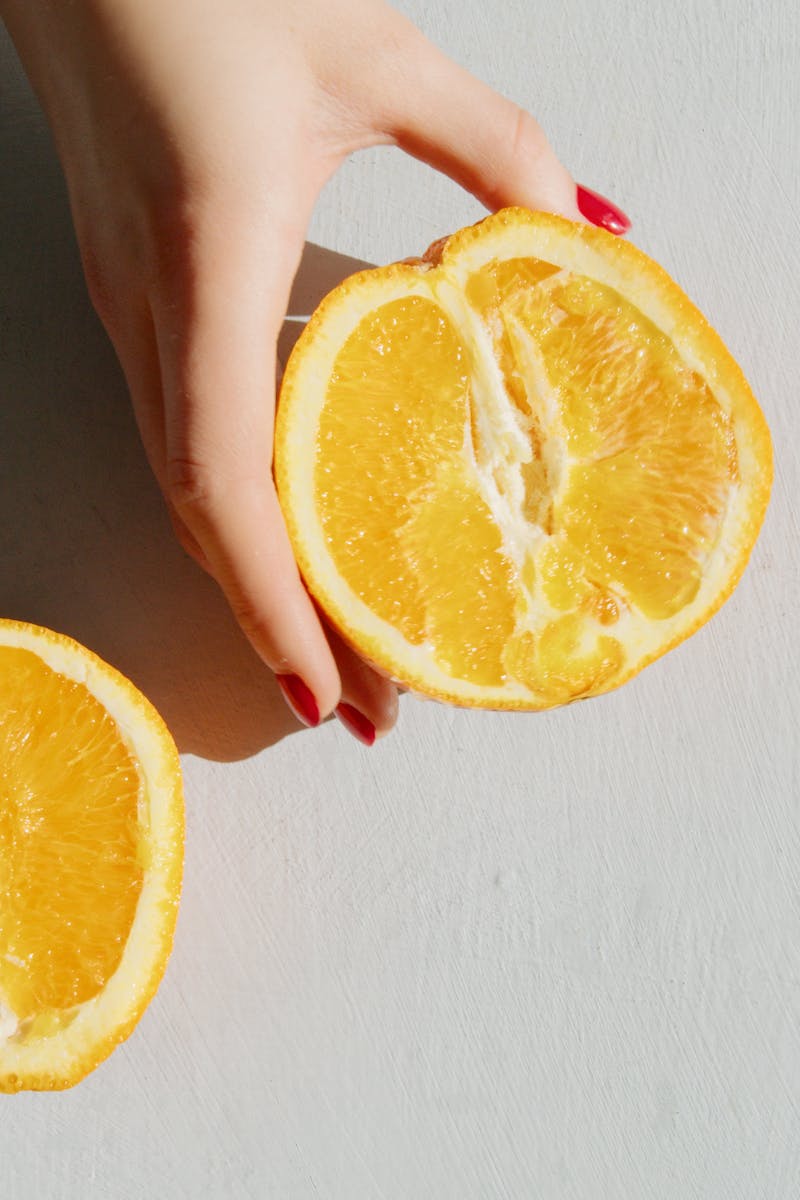 A hand holds vibrant orange slices in a sunlit flatlay, creating summer vibes.